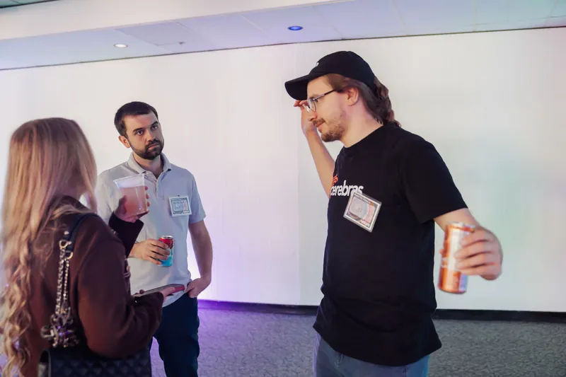 Three attendees with drinks in hand connect near a luminous display wall inside the Space Centre.