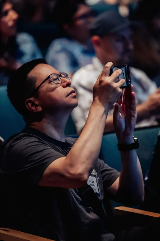 An audience member holds up a compact camera to capture the presentation from his seat in the planetarium theater.