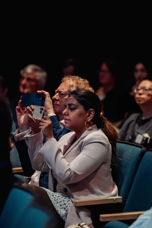 An audience member raises her phone to photograph the stage during the program.