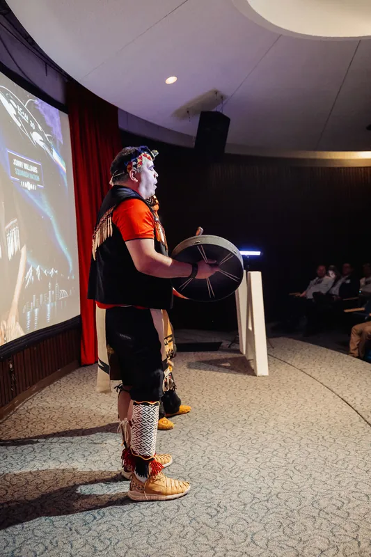 A Squamish Nation drummer performs solo inside the curved Space Centre theatre as seated attendees watch from the side.