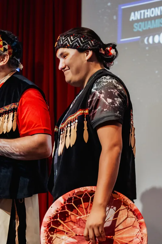 One of the Squamish Nation performers shares a warm, genuine smile between songs under the stage lights.