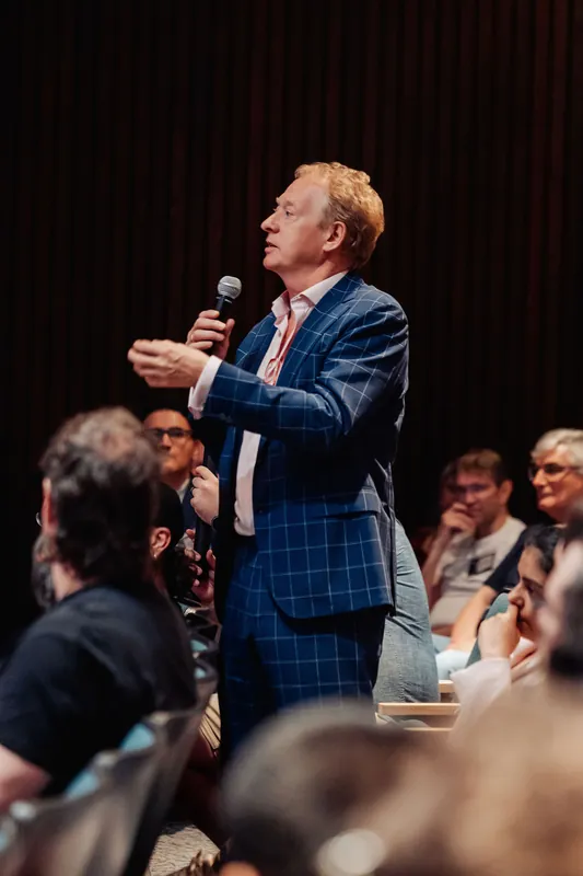 The speaker makes a point with an expressive hand gesture as the crowd stays fixed on him.