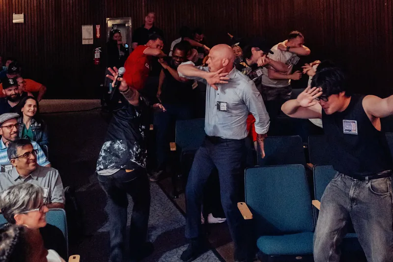 A spontaneous group movement activity breaks out among grinning rows of attendees in the Space Centre hall.