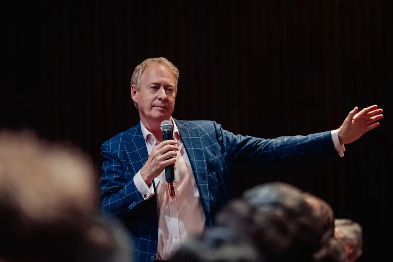 The speaker reaches toward the audience with an extended arm during an animated floor exchange.