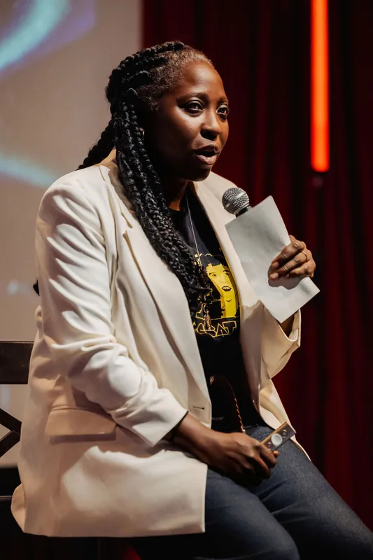 Anthonia Ogundele of Ethos Lab sits on stage in her cream blazer, notes in hand, speaking with quiet authority into the mic.