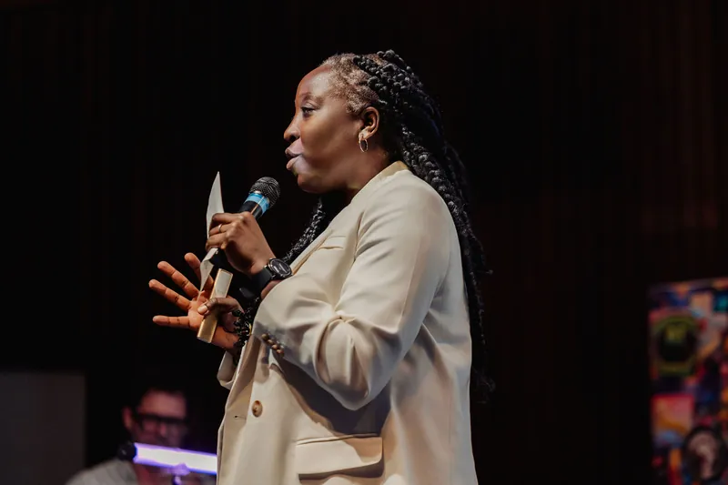 Anthonia Ogundele spreads both hands expressively while making a key point, her cream blazer catching the warm stage light.