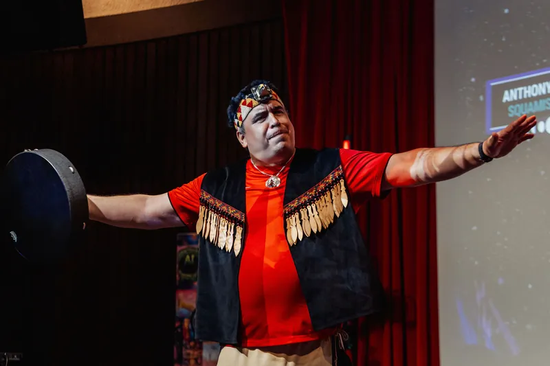 An Indigenous cultural performer stretches both arms wide in a commanding pose during the traditional opening ceremony.