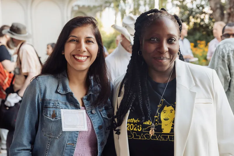 Two women pause for a warm photo together as the golden-hour reception hums behind them.