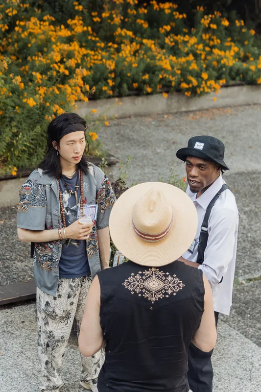 Three attendees in animated conversation outdoors at the Space Centre, a vivid wall of orange and yellow blooms behind them.
