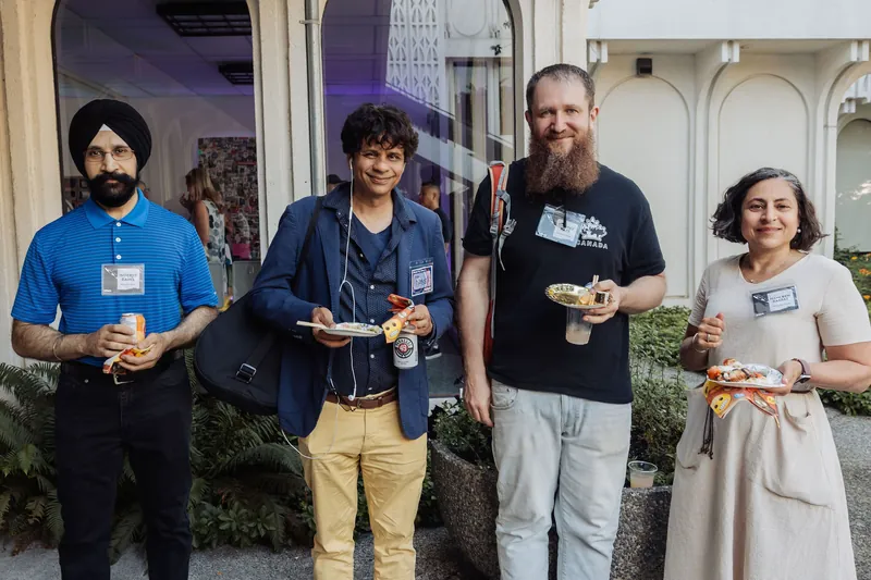 Four attendees balance food plates and lively conversation near the Space Centre entrance during the evening reception.