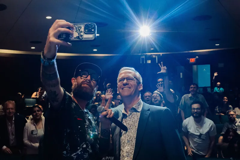 A slightly wider pull captures the infectious joy spreading through the audience as the group selfie continues under stage lights.