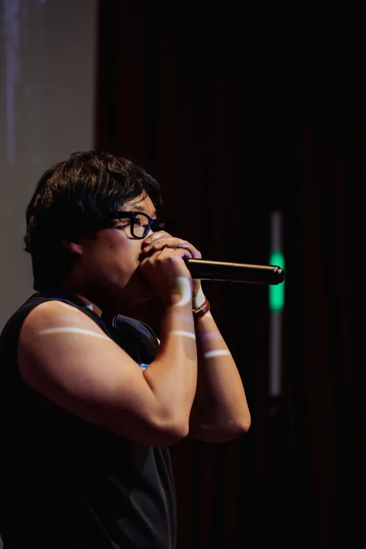 The performer's profile emerges from a dark background, a soft green stage light glowing in the wings.