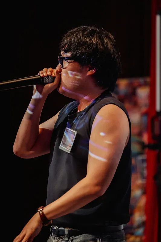 A tight profile shot captures the performer mid-verse, red curtains framing the darkened stage.