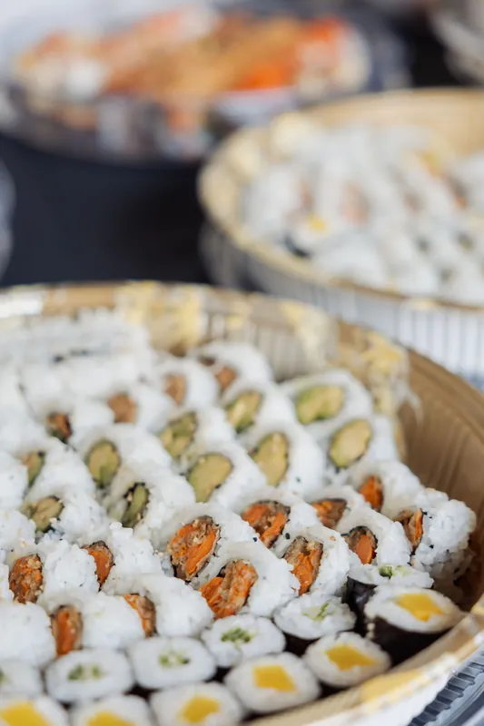 Multiple trays of colourful sushi rolls cover the catering table at the outdoor evening reception.