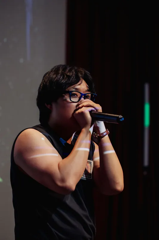 The performer looks upward mid-set, stage lighting cutting across their face with green color from behind.