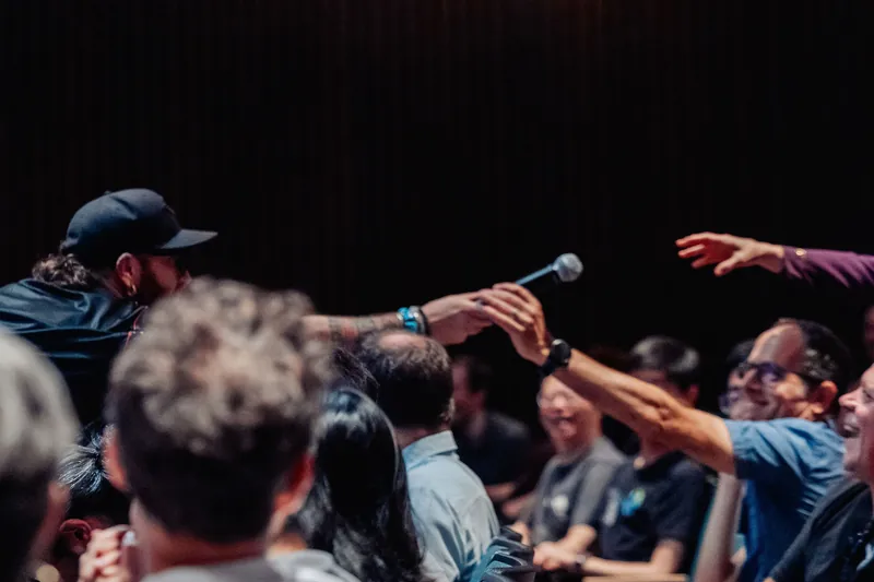 A roving mic handler stretches across rows to pass the microphone to an outstretched hand during a spirited Q&A.