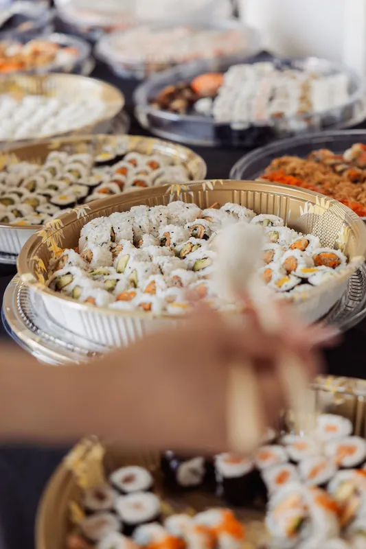 An attendee reaches chopsticks into a sushi tray piled high at the reception food spread.