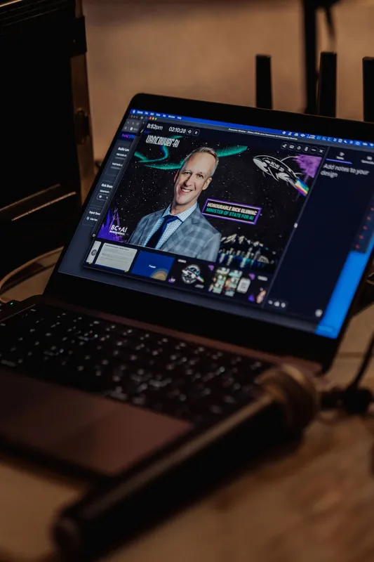 A close-up detail shot of a laptop screen open to what appears to be presentation production software, showing slide graphics in progress. A handheld microphone rests in the foreground on a dark surface.