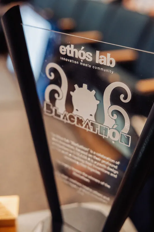 An Ethos Lab Blackathon acrylic sign sits on a table during the Vancouver AI Meetup.