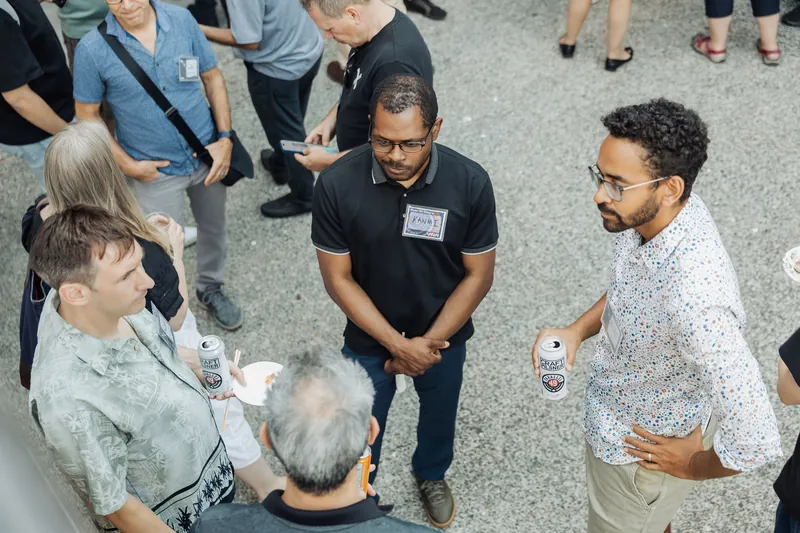 Attendees cluster in lively conversation on the outdoor plaza, drinks and name tags in hand.