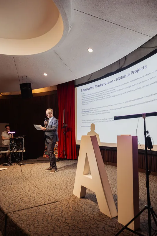 Bold AI letter props stand at stage front while a speaker presents in the background.