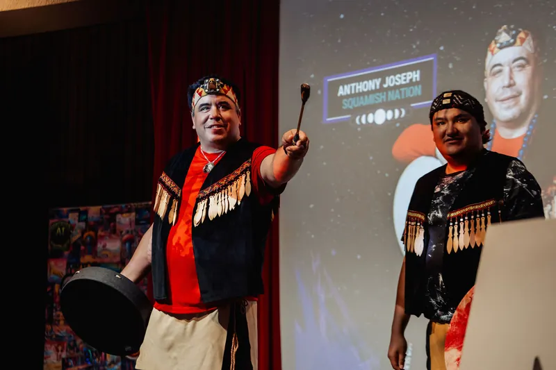 A performer raises a drum mallet skyward in a moment of energy during the Squamish Nation opening ceremony.