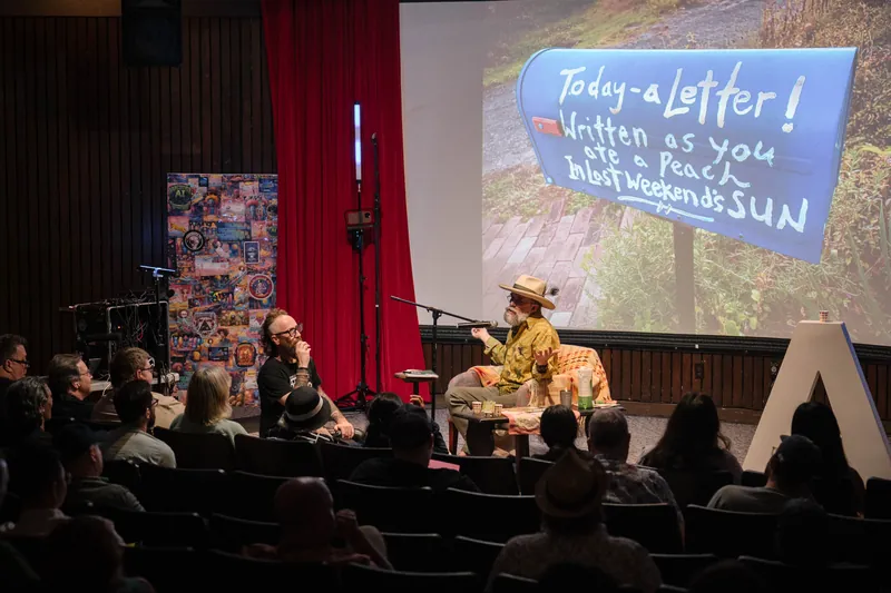 An on-stage conversation with Dave Olson — two chairs, mic, and a listening room — Soft focus on the crowd edge.