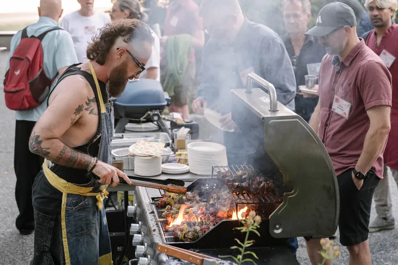 The grill cook raises both arms in celebration as smoke and flames rise from the BBQ.