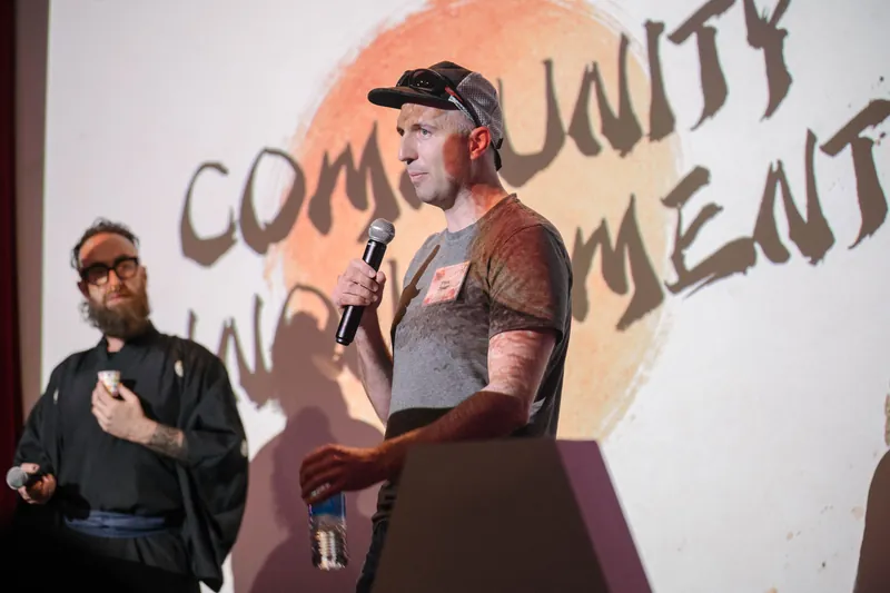Community members take the mic for announcements under the peach slide.