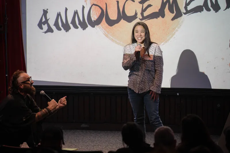 A community announcer shares updates from center stage — Closer on the mic.