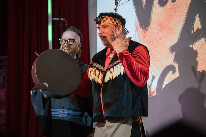 Welcome speakers share the stage — drum and mic catching the spotlight — Stage-left view.