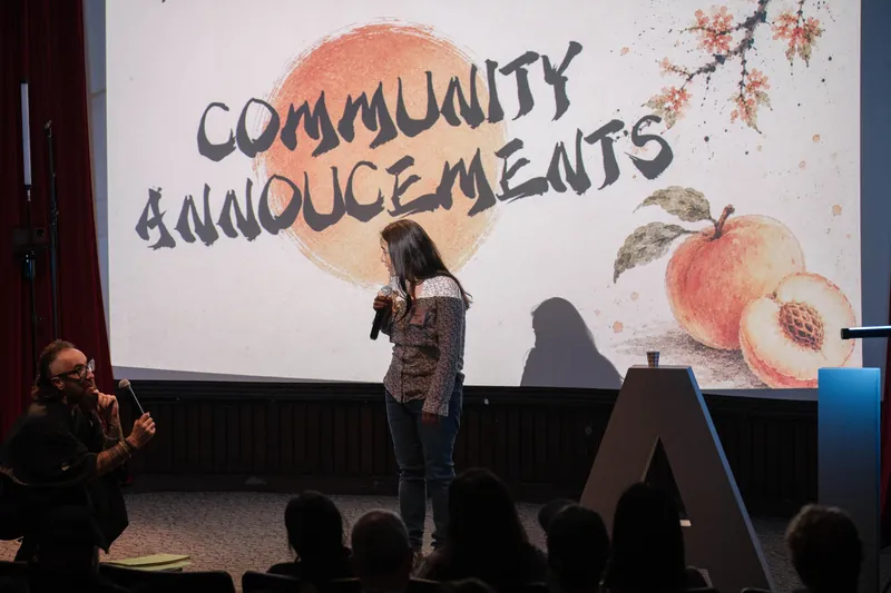 A community announcer shares updates from center stage — Stage-right view.