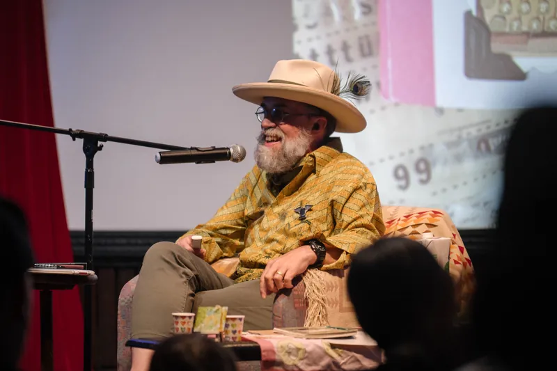 Dave Olson speaks from the armchair, gesturing as slides cycle behind him — Stage-right view.