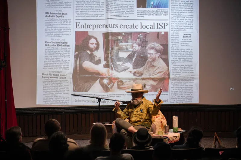 Dave Olson leans into storytelling — clippings, collages, and handwritten notes on screen — Soft focus on the crowd edge.