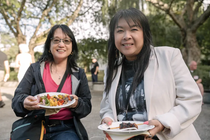 Guests smile for the camera with plates of BBQ on the outdoor patio — Stage-left view.