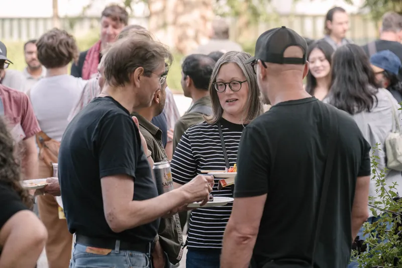Crowds fill the courtyard for outdoor networking in the late-day light — From the aisle.