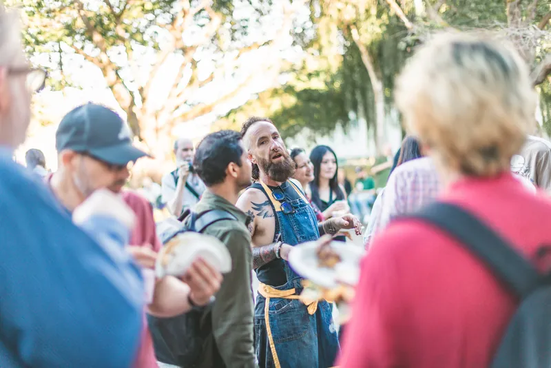 A guest talks with friends, plate in hand, at the barbecue.