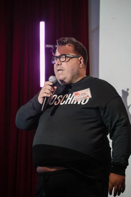 A community announcer in a black hoodie speaks into the mic during announcements.