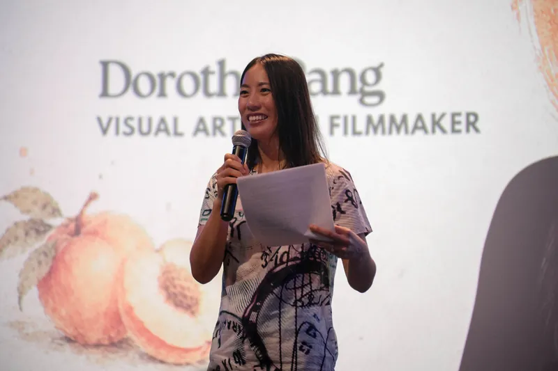 Dorothy Pang smiles at the room, mic and notes in hand, under her title slide.