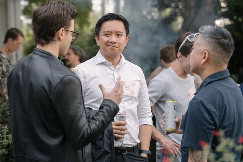 Candid conversations spill across the outdoor mixer before the program starts — Closer on the mic.