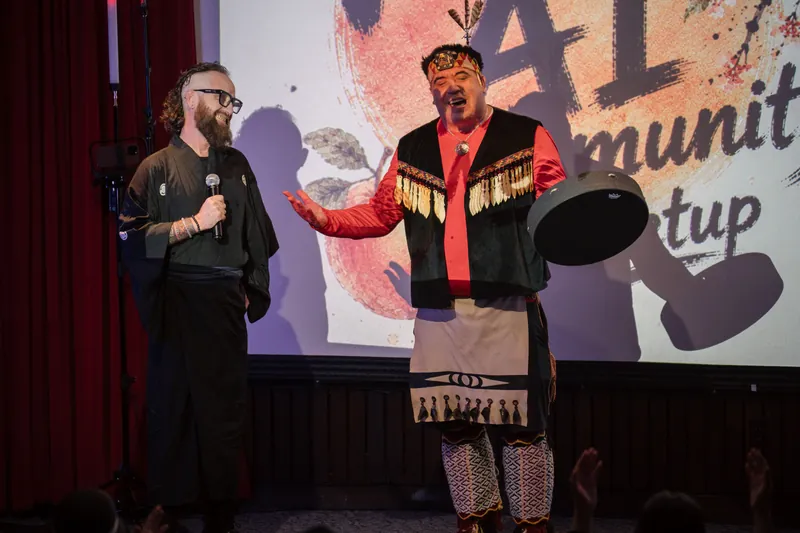Welcome performers share the stage — one holding a traditional frame drum — under the meetup title slide.