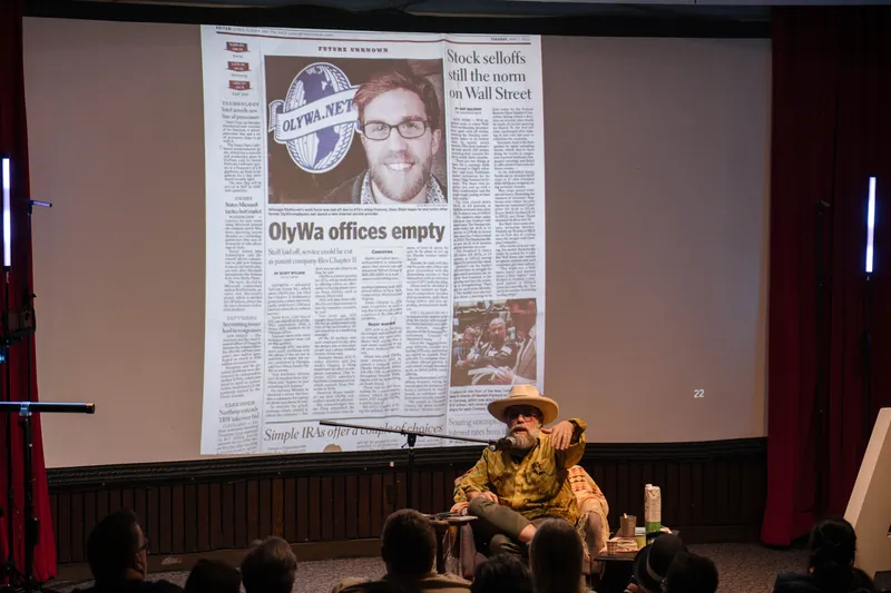 Dave Olson leans into storytelling — clippings, collages, and handwritten notes on screen — Stage-left view.