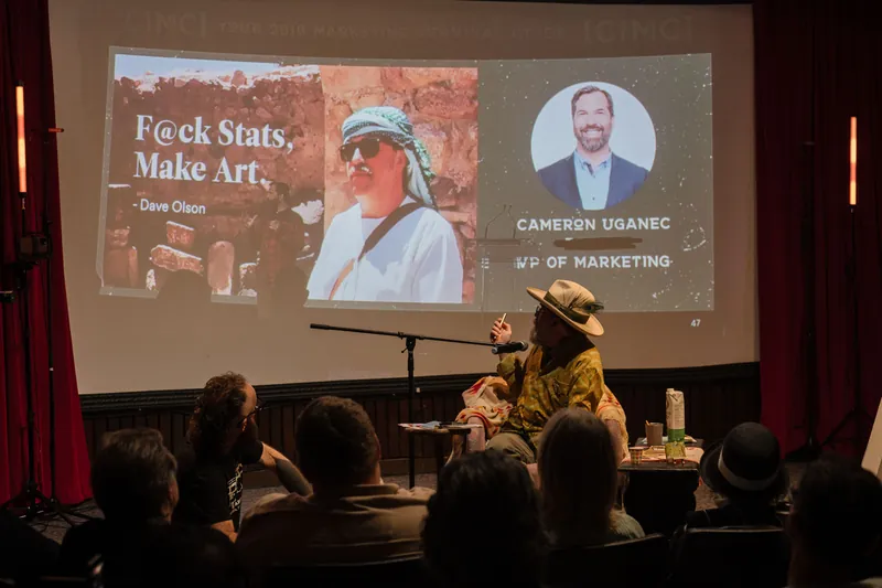 Dave Olson continues from the armchair as denser text and photo slides roll — Stage-left view.
