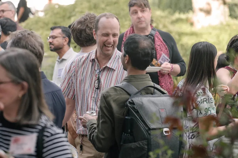 Crowds fill the courtyard for outdoor networking in the late-day light — Closer on the mic.