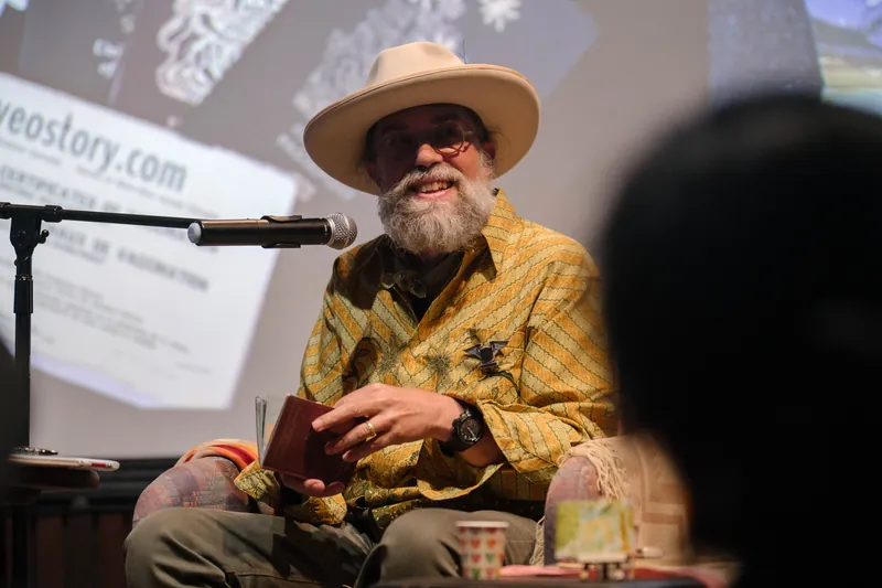 Dave Olson continues from the armchair as denser text and photo slides roll — Stage-right view.