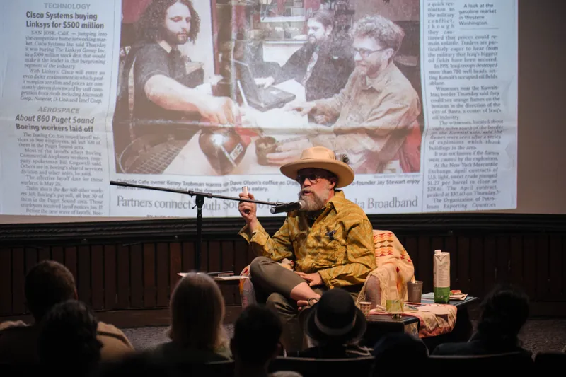 Dave Olson leans into storytelling — clippings, collages, and handwritten notes on screen — Closer on the mic.