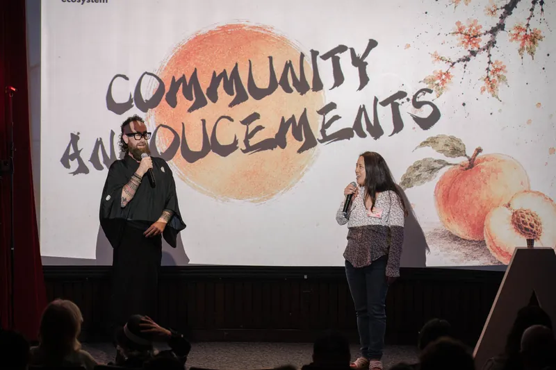More community announcements roll on — mic handoffs and short stage spots — Wider angle.