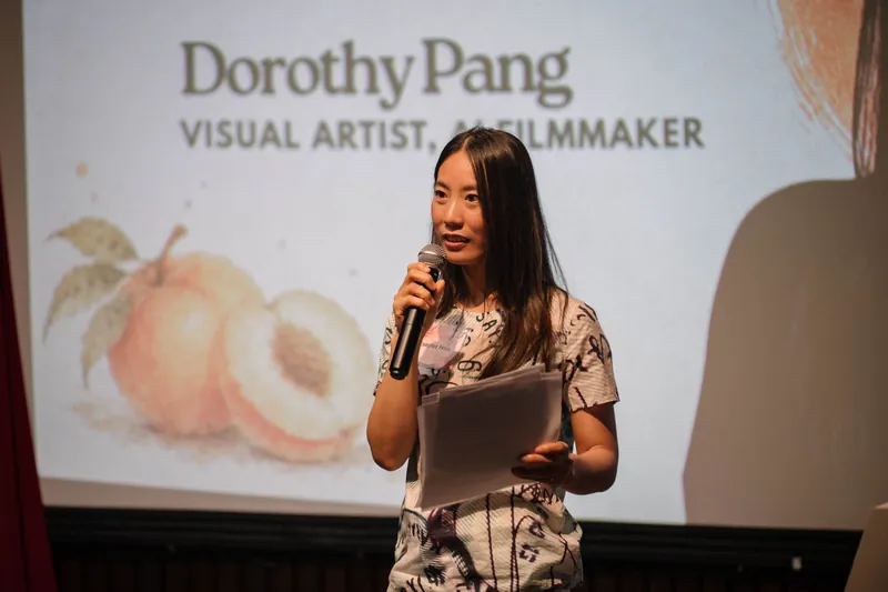 Dorothy Pang presents from mid-stage, patterned top catching the spotlight.