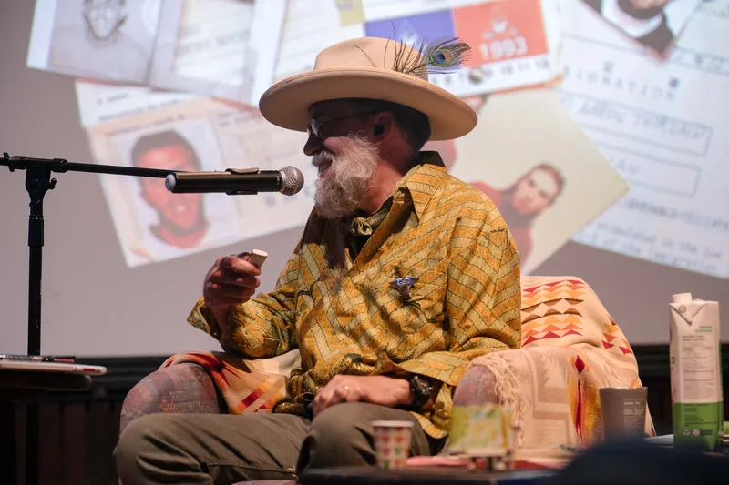 Dave Olson leans into storytelling — clippings, collages, and handwritten notes on screen — Stage-right view.