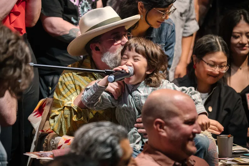 A tender on-stage moment as Dave Olson leans in toward a child at the mic.